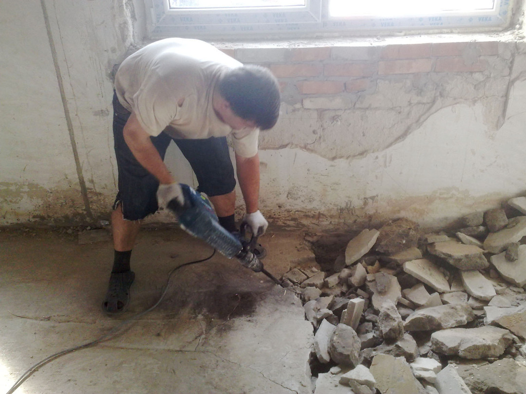 A man with a puncher dismantles the floor screed